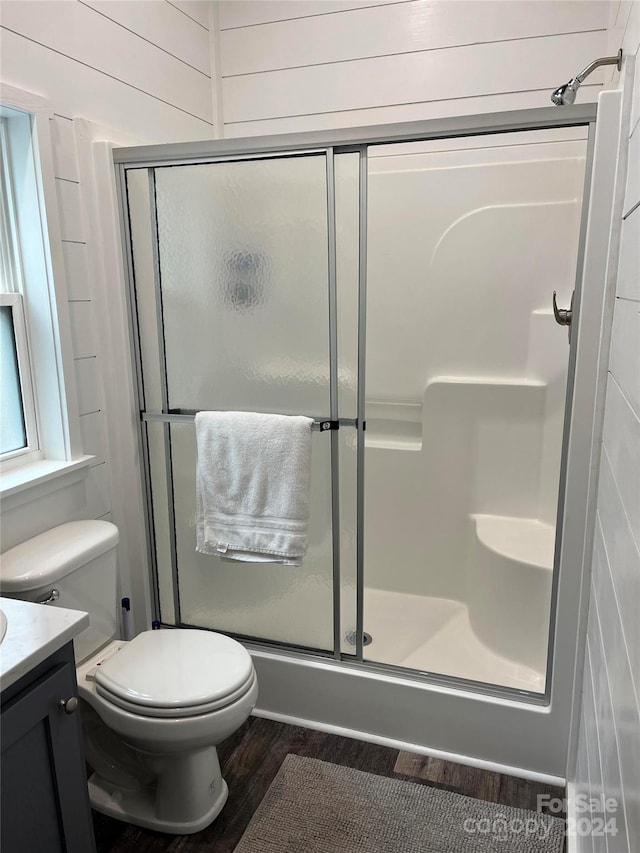 bathroom with hardwood / wood-style floors, a shower with door, toilet, and vanity