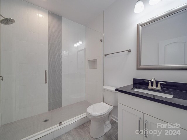 full bathroom with toilet, vanity, wood finished floors, and tiled shower