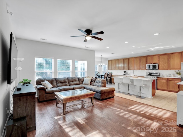 living room featuring ceiling fan with notable chandelier and light wood-type flooring