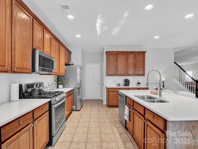 kitchen featuring light tile patterned floors, a center island with sink, stainless steel appliances, tasteful backsplash, and sink