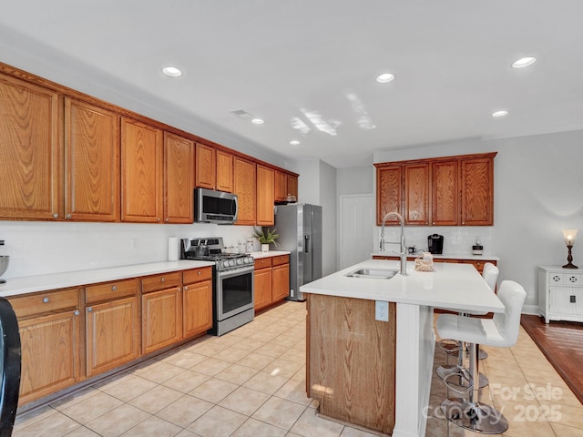 kitchen with light tile patterned floors, stainless steel appliances, a kitchen island with sink, a kitchen breakfast bar, and sink