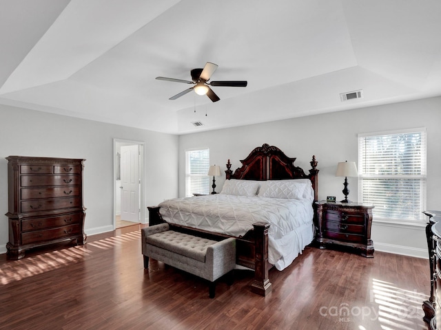 bedroom with dark hardwood / wood-style floors, ceiling fan, a raised ceiling, and multiple windows