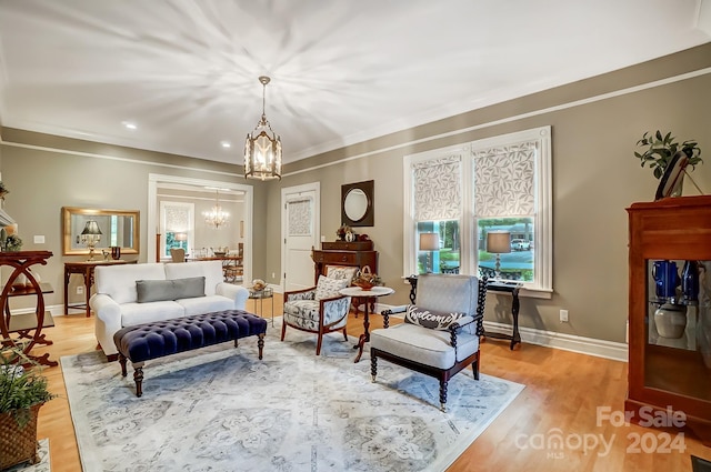 living area featuring crown molding, an inviting chandelier, and light wood-type flooring