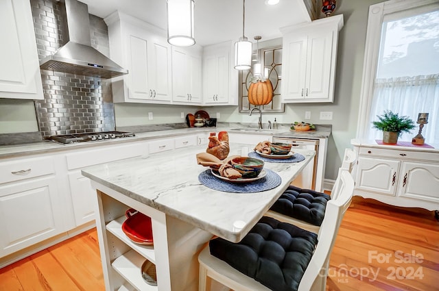 kitchen with wall chimney exhaust hood, hanging light fixtures, white dishwasher, light wood-type flooring, and white cabinetry