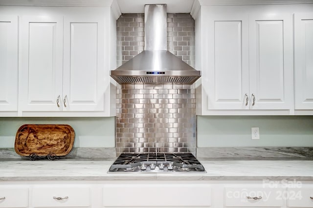 kitchen with wall chimney range hood, white cabinets, backsplash, and stainless steel gas cooktop