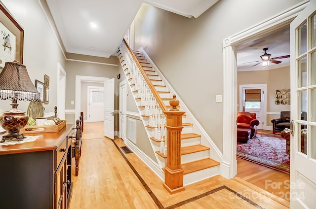 staircase with ceiling fan, wood-type flooring, and ornamental molding