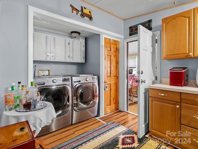 laundry area featuring light wood-type flooring, washer and clothes dryer, crown molding, and cabinets