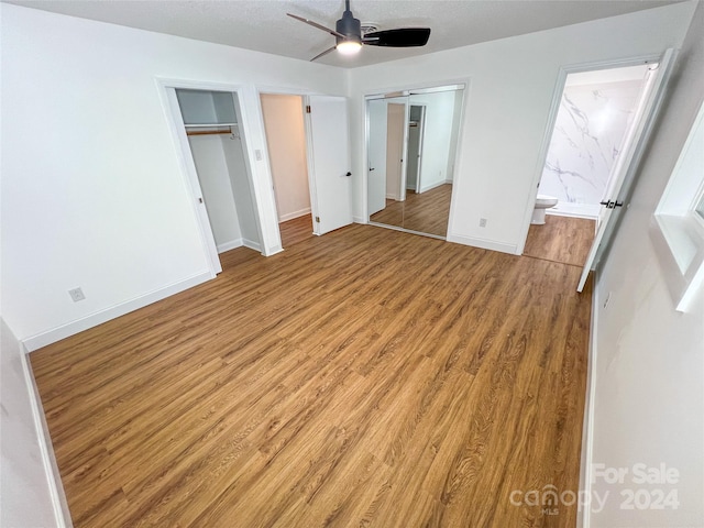 unfurnished bedroom with ensuite bath, ceiling fan, multiple closets, and light wood-type flooring