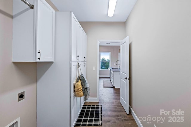 laundry room with cabinet space, baseboards, dark wood finished floors, electric dryer hookup, and a sink