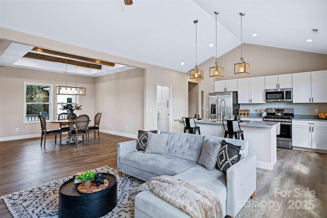 living area with baseboards, visible vents, a tray ceiling, and wood finished floors