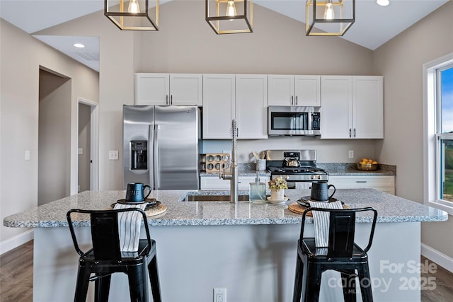 kitchen with dark wood-type flooring, white cabinetry, vaulted ceiling, appliances with stainless steel finishes, and a center island with sink