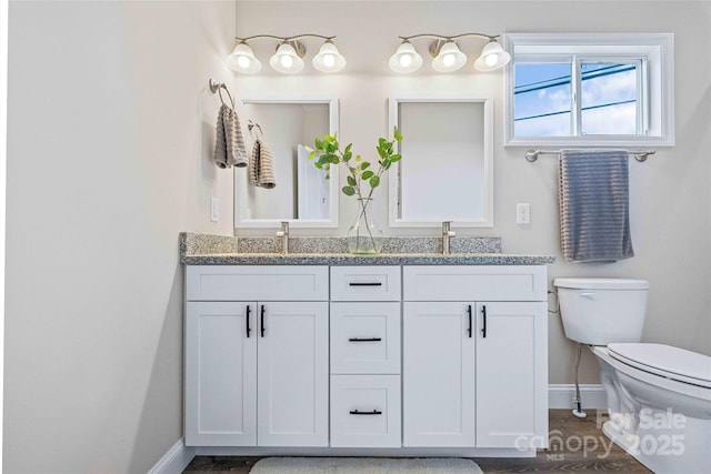 full bathroom with baseboards, a sink, toilet, and double vanity