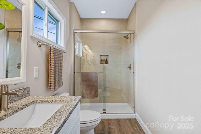 full bathroom with a stall shower, baseboards, toilet, wood finished floors, and vanity