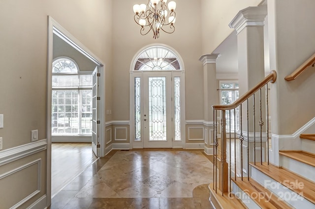 foyer entrance featuring a high ceiling, decorative columns, a notable chandelier, and plenty of natural light