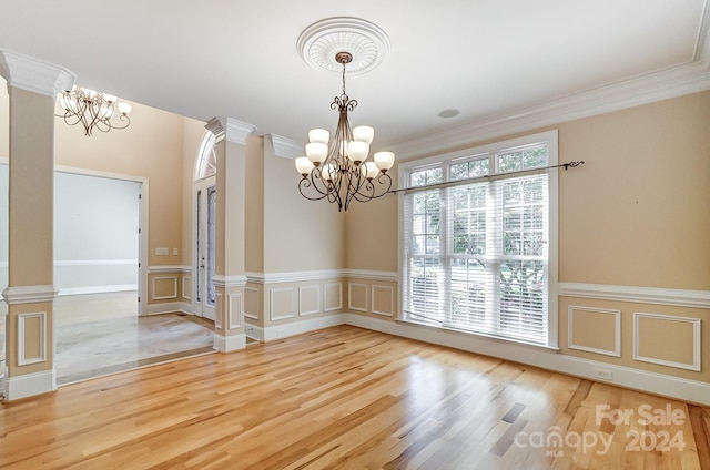 unfurnished dining area with a notable chandelier, hardwood / wood-style flooring, crown molding, and decorative columns