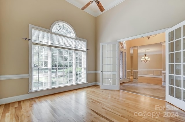 spare room featuring hardwood / wood-style floors, french doors, ceiling fan with notable chandelier, a high ceiling, and ornate columns