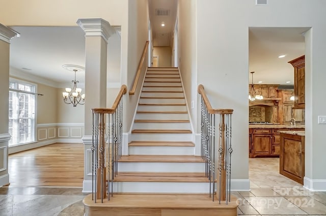 stairs with hardwood / wood-style floors, an inviting chandelier, crown molding, and ornate columns