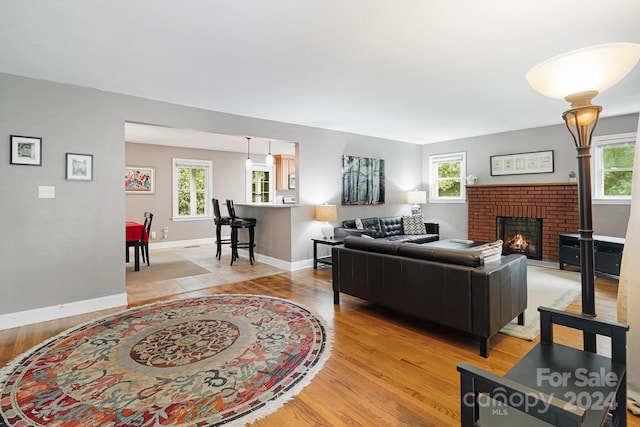 living room featuring a wealth of natural light, light hardwood / wood-style flooring, and a brick fireplace