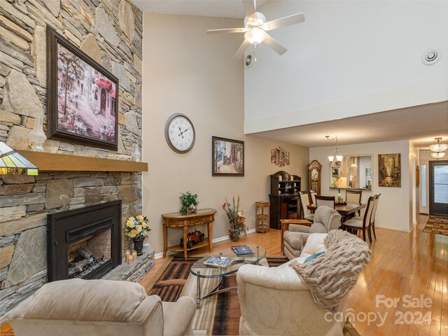 living room with a stone fireplace, ceiling fan with notable chandelier, and hardwood / wood-style floors