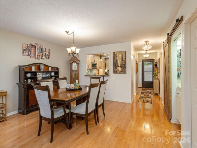 dining area featuring a barn door, a textured ceiling, light hardwood / wood-style flooring, and a notable chandelier