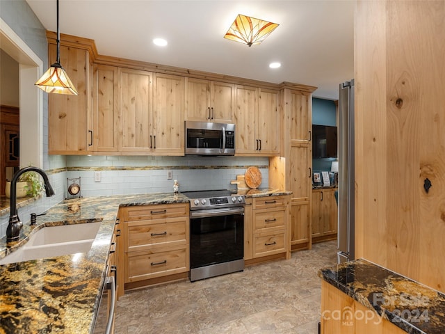 kitchen featuring appliances with stainless steel finishes, light brown cabinets, decorative light fixtures, dark stone counters, and sink