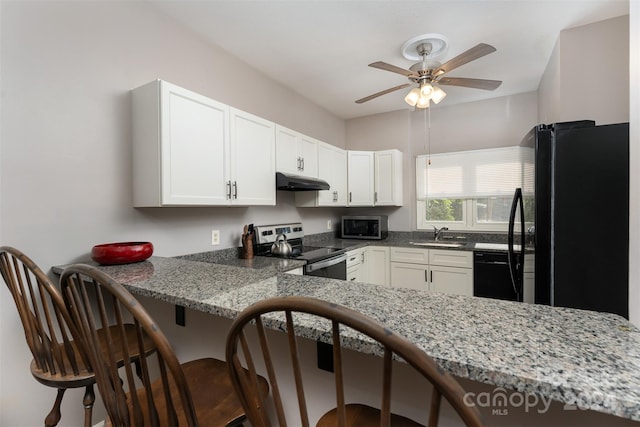 kitchen featuring kitchen peninsula, a kitchen breakfast bar, light stone counters, black appliances, and white cabinets