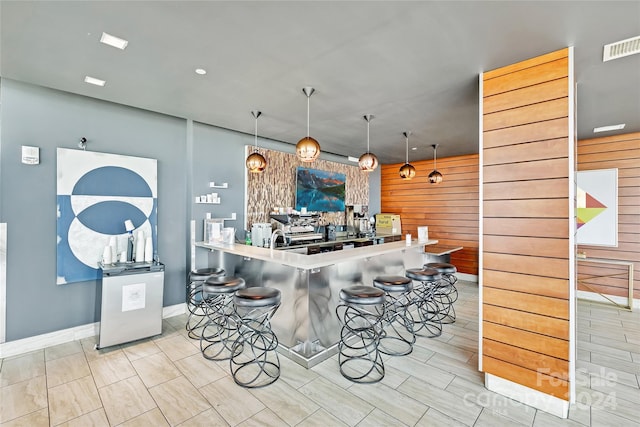 kitchen featuring sink, wood walls, kitchen peninsula, a kitchen bar, and hanging light fixtures