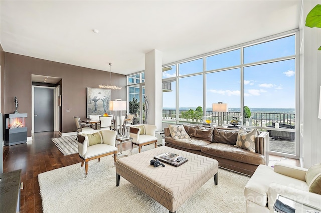 living room with an inviting chandelier, floor to ceiling windows, a water view, and dark wood-type flooring