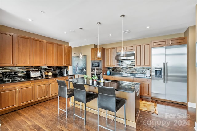 kitchen featuring a kitchen breakfast bar, a kitchen island, built in appliances, pendant lighting, and wood-type flooring