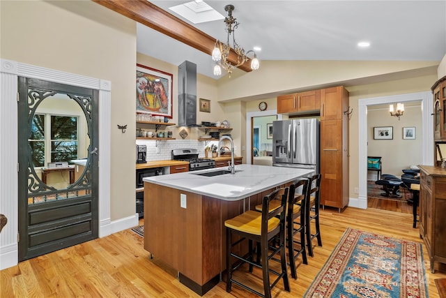 kitchen with stainless steel appliances, a center island with sink, vaulted ceiling with skylight, decorative light fixtures, and light wood-type flooring