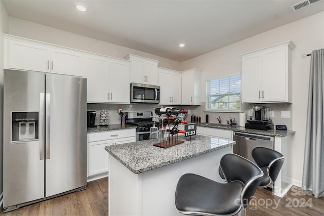 kitchen featuring a center island, white cabinetry, stainless steel appliances, dark hardwood / wood-style flooring, and light stone countertops