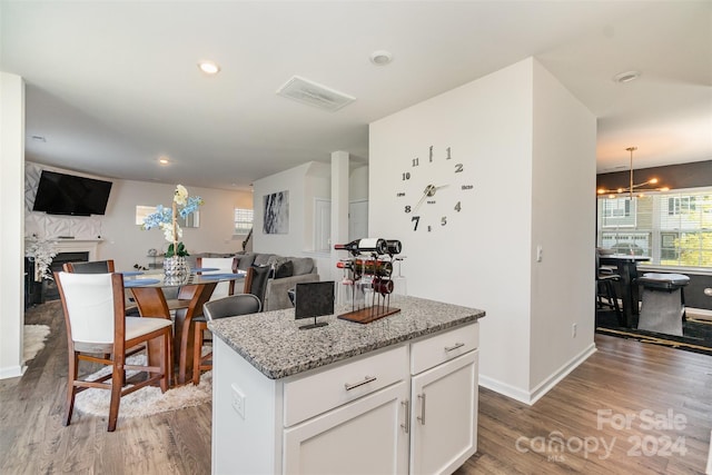 kitchen featuring light stone counters, white cabinets, pendant lighting, wood-type flooring, and a center island