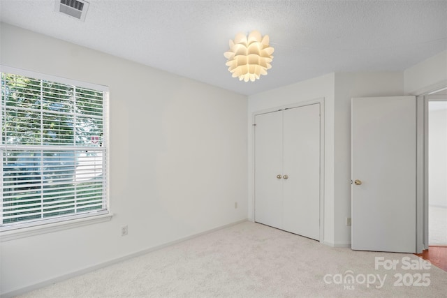 unfurnished bedroom featuring light colored carpet, a textured ceiling, and a closet