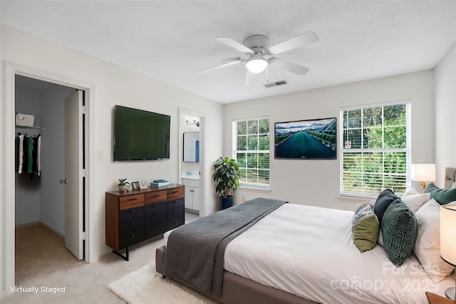 bedroom featuring multiple windows, a walk in closet, light carpet, and ensuite bath