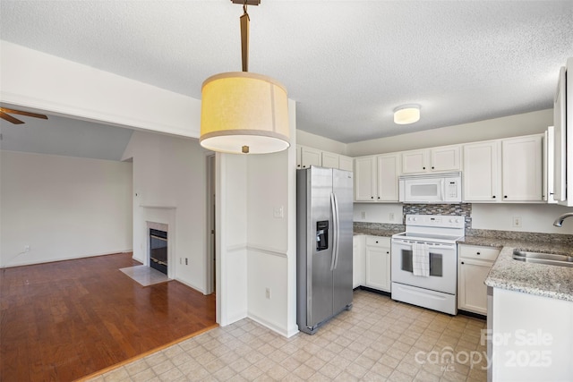 kitchen featuring pendant lighting, white cabinetry, sink, a tiled fireplace, and white appliances