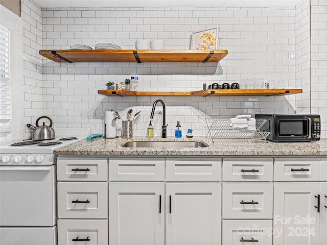 kitchen featuring white range, sink, white cabinets, light stone counters, and tasteful backsplash