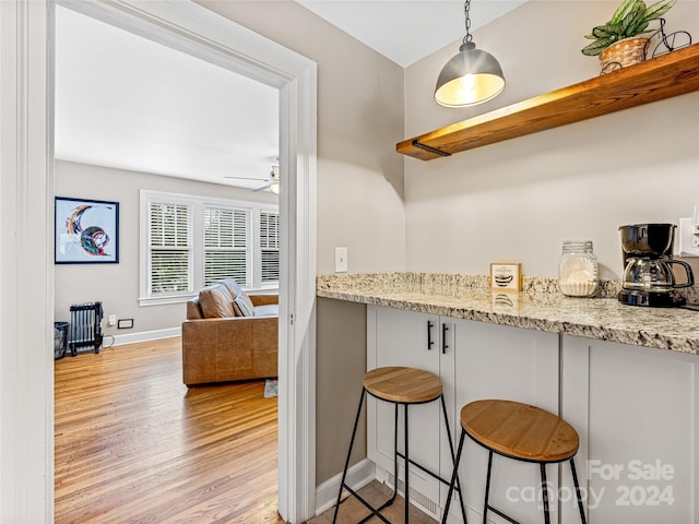 kitchen with a kitchen breakfast bar, light stone counters, light wood-type flooring, and ceiling fan