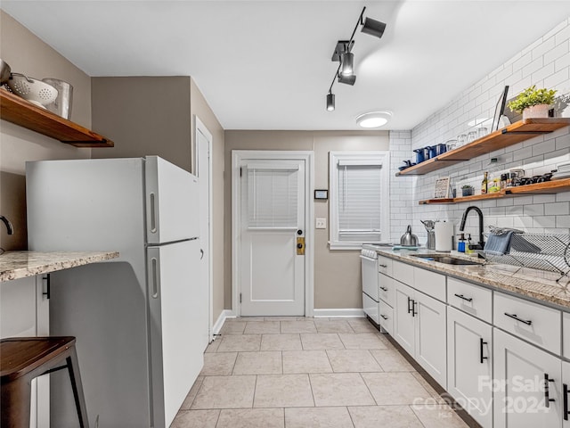 kitchen with sink, white cabinetry, white fridge, light stone counters, and decorative backsplash