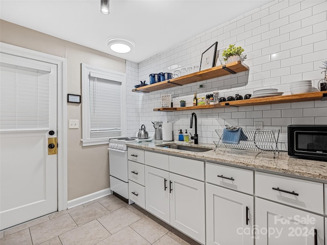 kitchen with decorative backsplash, white range oven, sink, light stone countertops, and white cabinets