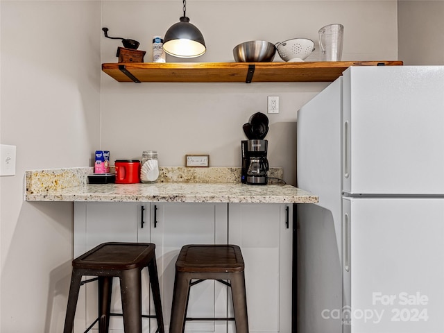 kitchen featuring light stone countertops, a breakfast bar area, white refrigerator, and hanging light fixtures