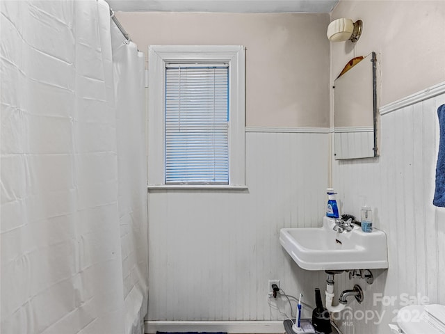 bathroom featuring toilet, a shower with curtain, sink, and wooden walls