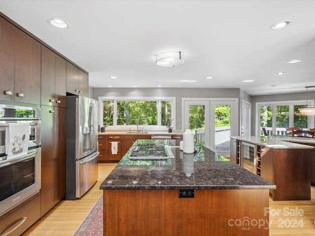 kitchen with light hardwood / wood-style floors, dark stone counters, sink, stainless steel appliances, and a center island