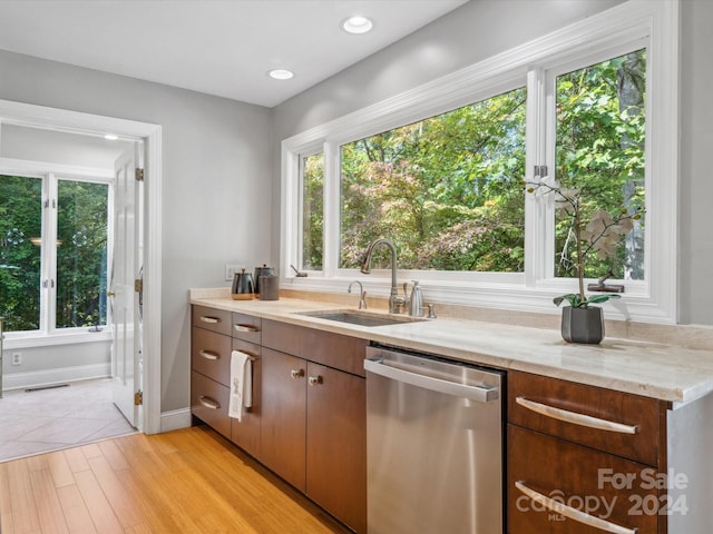 kitchen featuring light stone countertops, light wood-type flooring, sink, and stainless steel dishwasher