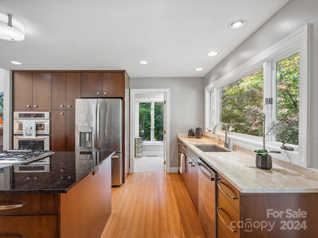 kitchen with stainless steel appliances, light wood-type flooring, sink, and a healthy amount of sunlight