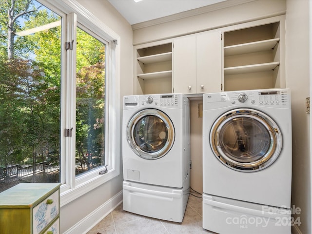 clothes washing area featuring light tile patterned flooring, washer and dryer, and cabinets