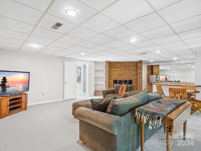 carpeted living room with a brick fireplace, a drop ceiling, and built in shelves