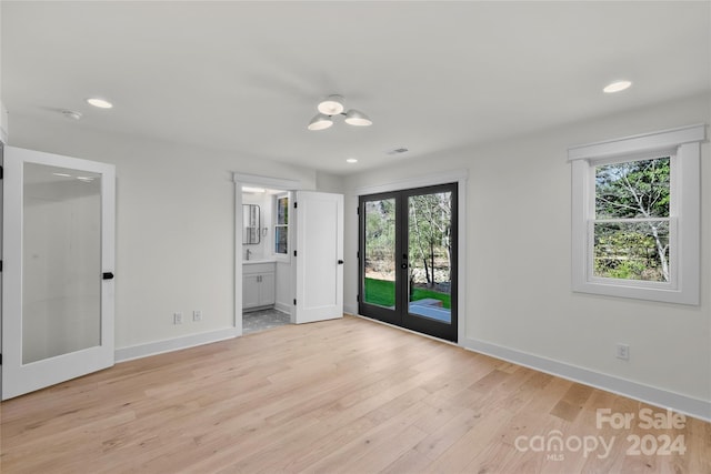 unfurnished bedroom featuring multiple windows, french doors, ensuite bath, and light hardwood / wood-style floors