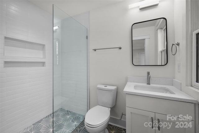 bathroom with a tile shower, tile patterned floors, vanity, and toilet