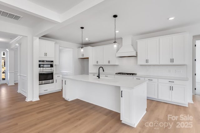 kitchen with a center island with sink, visible vents, white cabinets, custom exhaust hood, and light countertops