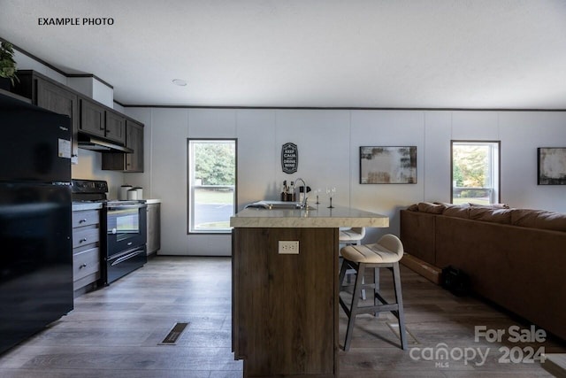 kitchen with black appliances, a kitchen bar, a kitchen island with sink, dark hardwood / wood-style floors, and sink